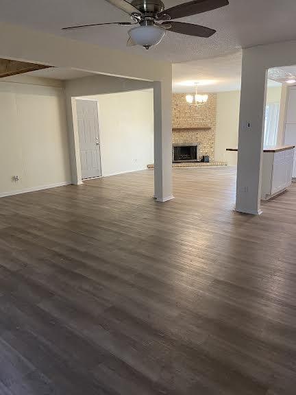 unfurnished living room with ceiling fan with notable chandelier, dark hardwood / wood-style floors, and a fireplace