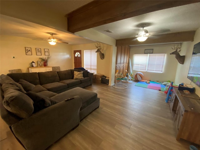 living room with wood finished floors, visible vents, a ceiling fan, and beam ceiling