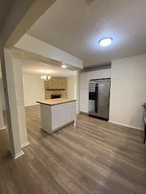 kitchen featuring a textured ceiling, a chandelier, stainless steel fridge, hardwood / wood-style floors, and white cabinetry