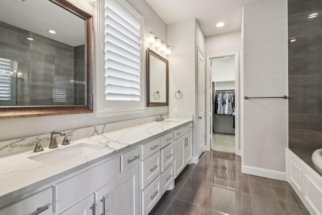 full bath featuring a garden tub, a sink, baseboards, double vanity, and a walk in closet