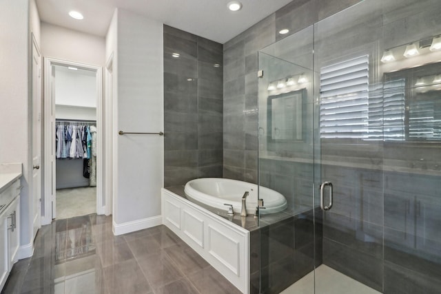 full bath with a walk in closet, a garden tub, vanity, a shower stall, and baseboards