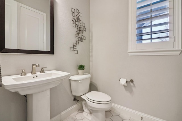 half bathroom featuring a sink, tile patterned flooring, toilet, and baseboards