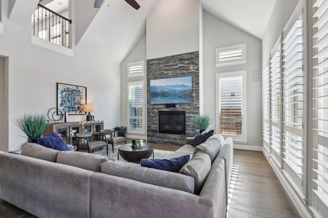 living room featuring a towering ceiling, dark wood-type flooring, ceiling fan, and a fireplace