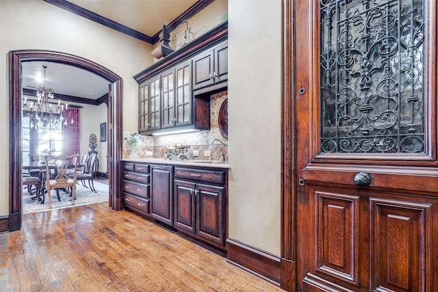 bar with sink, decorative backsplash, crown molding, and light hardwood / wood-style flooring