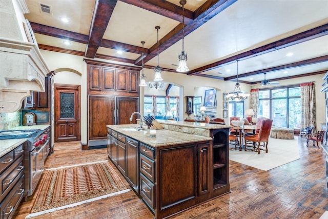 kitchen featuring dark hardwood / wood-style floors, high end stainless steel range oven, an island with sink, hanging light fixtures, and sink