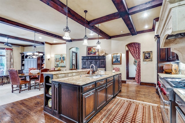 kitchen with high end range, decorative light fixtures, a center island with sink, dark hardwood / wood-style flooring, and dark brown cabinets