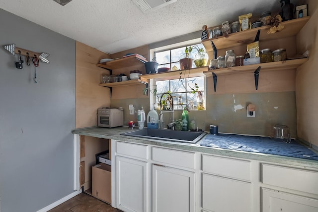 kitchen with a textured ceiling, dark tile patterned floors, sink, white cabinetry, and tasteful backsplash