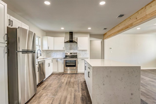 kitchen featuring stainless steel appliances, wall chimney range hood, hardwood / wood-style flooring, and white cabinetry