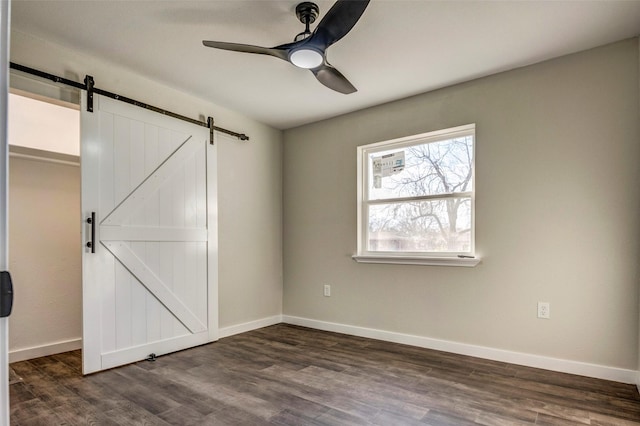 unfurnished bedroom with a closet, a barn door, ceiling fan, dark wood-type flooring, and a walk in closet