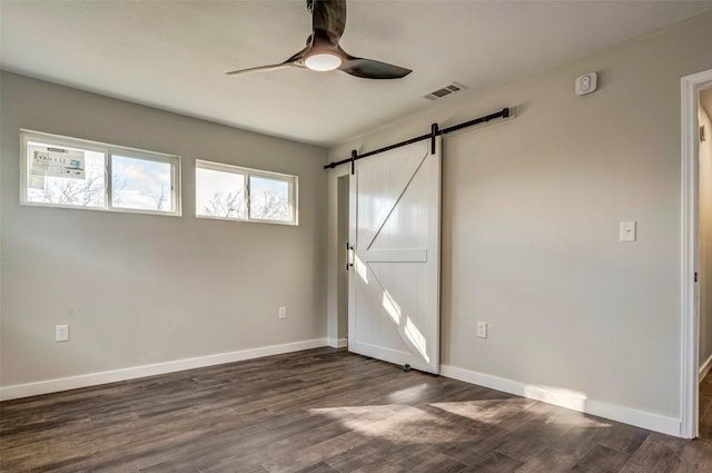 unfurnished bedroom featuring ceiling fan, dark hardwood / wood-style flooring, and a barn door