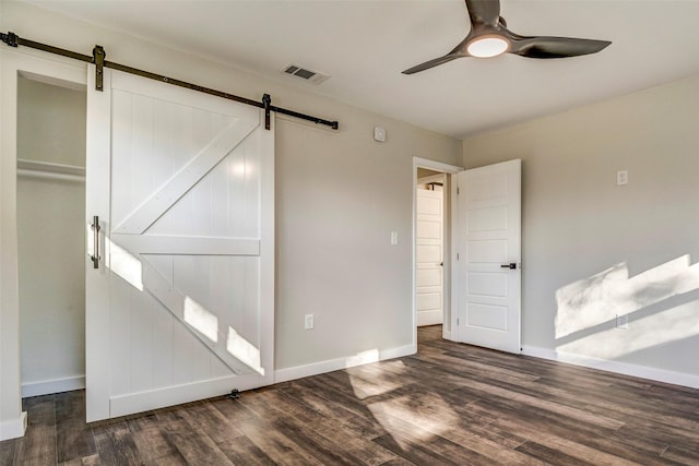 empty room featuring dark wood-type flooring, ceiling fan, and a barn door