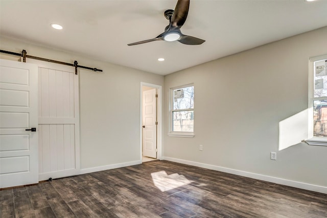 unfurnished bedroom with ceiling fan, a barn door, and dark hardwood / wood-style floors