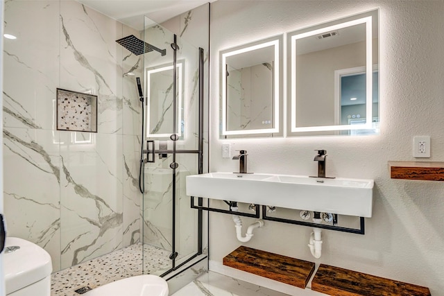 bathroom with toilet, a tile shower, and sink