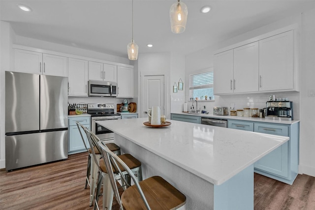 kitchen with hanging light fixtures, a kitchen island, stainless steel appliances, decorative backsplash, and white cabinets