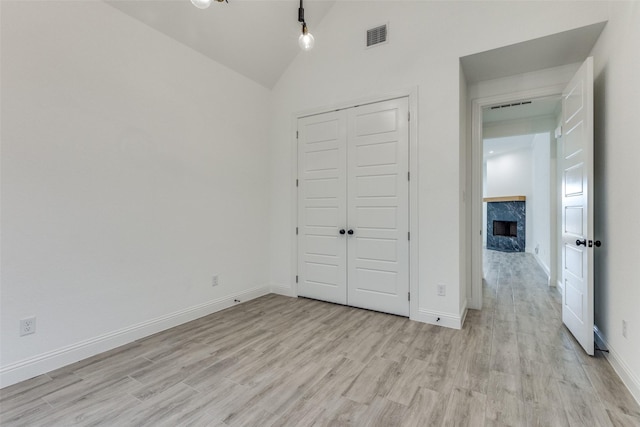 unfurnished bedroom featuring light wood-type flooring, a closet, vaulted ceiling, and a fireplace