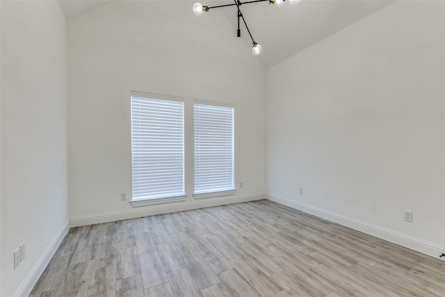 unfurnished room with high vaulted ceiling, a notable chandelier, and light hardwood / wood-style flooring