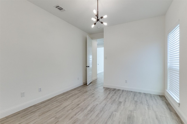 unfurnished room featuring a notable chandelier and light wood-type flooring