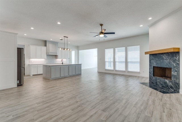 unfurnished living room featuring a fireplace, ceiling fan, crown molding, and light hardwood / wood-style flooring