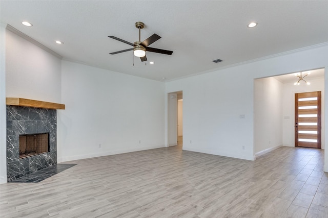 unfurnished living room with ceiling fan with notable chandelier, a premium fireplace, ornamental molding, and light hardwood / wood-style flooring