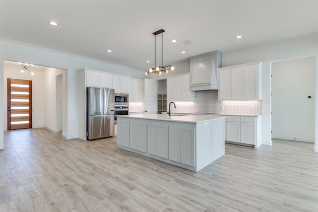 kitchen featuring stainless steel appliances, custom exhaust hood, a kitchen island with sink, and white cabinets