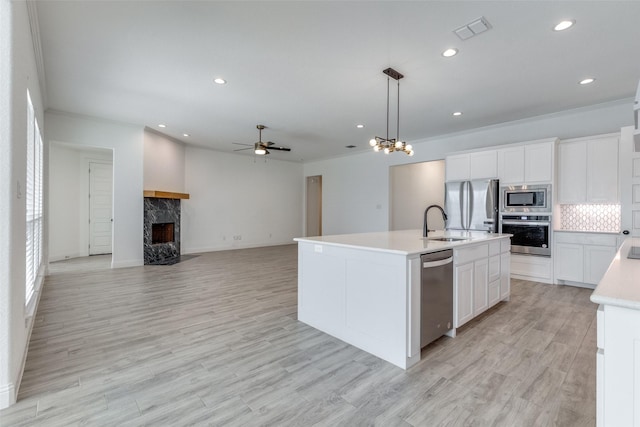 kitchen featuring hanging light fixtures, stainless steel appliances, a center island with sink, decorative backsplash, and white cabinets