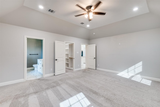 unfurnished bedroom featuring light carpet, connected bathroom, ceiling fan, a closet, and a walk in closet