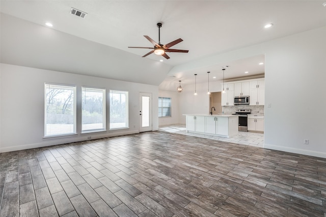 unfurnished living room featuring ceiling fan, vaulted ceiling, and sink