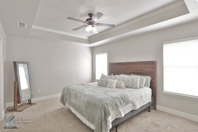 carpeted bedroom with a tray ceiling, crown molding, and ceiling fan