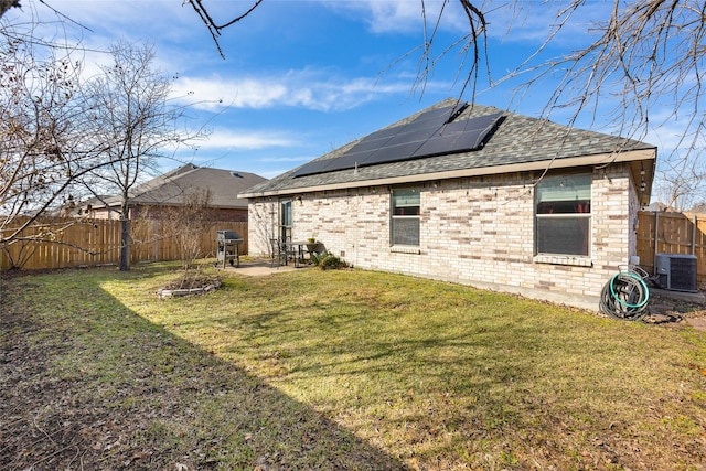 rear view of house with solar panels, central AC unit, and a yard