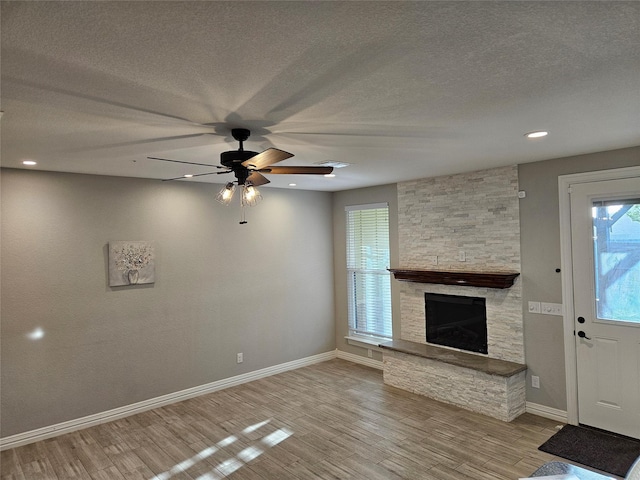 unfurnished living room with ceiling fan, light wood-type flooring, a stone fireplace, and a textured ceiling