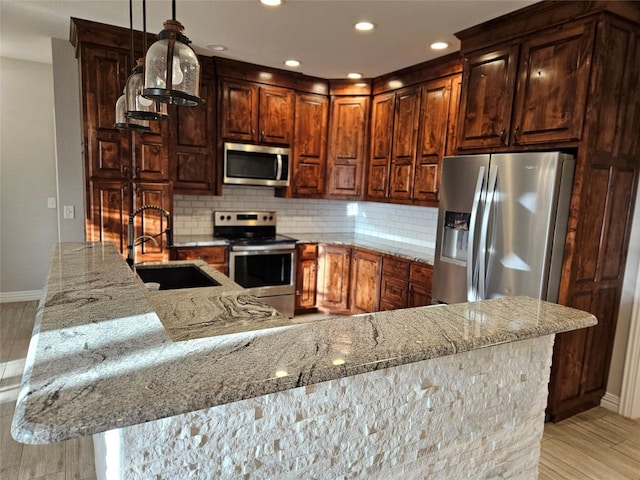 kitchen featuring pendant lighting, stainless steel appliances, light hardwood / wood-style floors, sink, and backsplash