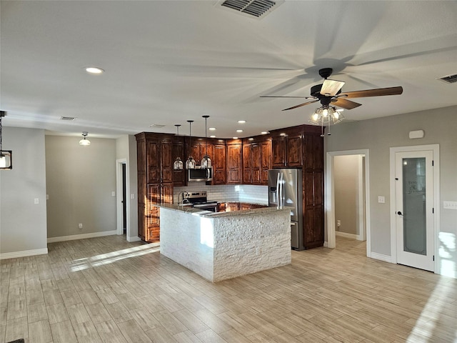 kitchen featuring decorative light fixtures, stainless steel appliances, light hardwood / wood-style floors, ceiling fan, and light stone counters