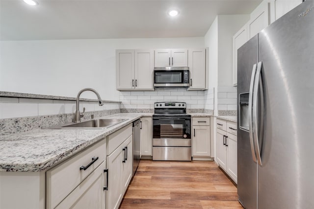 kitchen featuring sink, light hardwood / wood-style flooring, white cabinetry, stainless steel appliances, and tasteful backsplash