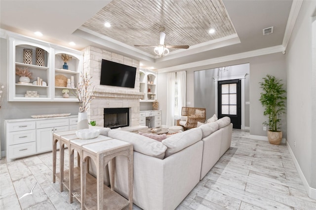 living room featuring ceiling fan, ornamental molding, a raised ceiling, and a stone fireplace