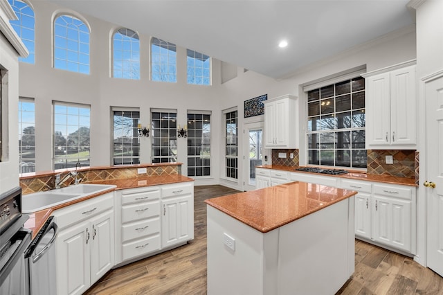 kitchen with white cabinets, stainless steel gas cooktop, backsplash, and a center island