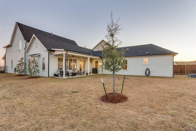 back house at dusk with a patio and a lawn