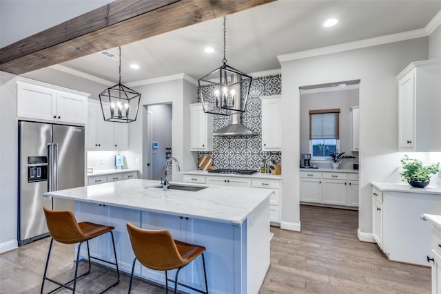 kitchen with stainless steel appliances, sink, white cabinets, light stone countertops, and a center island with sink