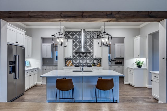 kitchen with stainless steel appliances, an island with sink, wall chimney range hood, a breakfast bar, and white cabinetry