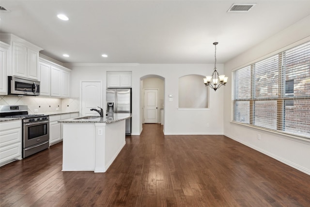 kitchen with stainless steel appliances, white cabinets, light stone countertops, a center island with sink, and pendant lighting