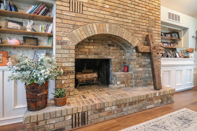 living room with a brick fireplace, built in features, and hardwood / wood-style flooring