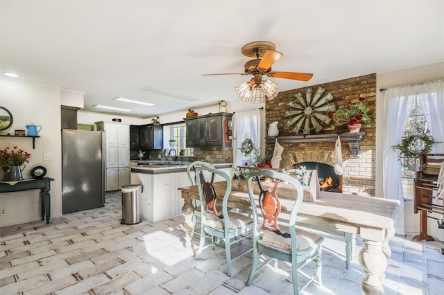 dining space with brick wall, a brick fireplace, ceiling fan, and sink