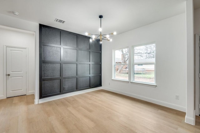 spare room featuring a chandelier and light hardwood / wood-style flooring