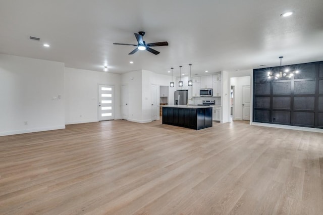 unfurnished living room featuring ceiling fan with notable chandelier and light hardwood / wood-style flooring