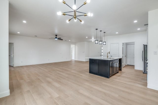 kitchen featuring decorative light fixtures, a center island with sink, sink, stainless steel fridge, and ceiling fan with notable chandelier