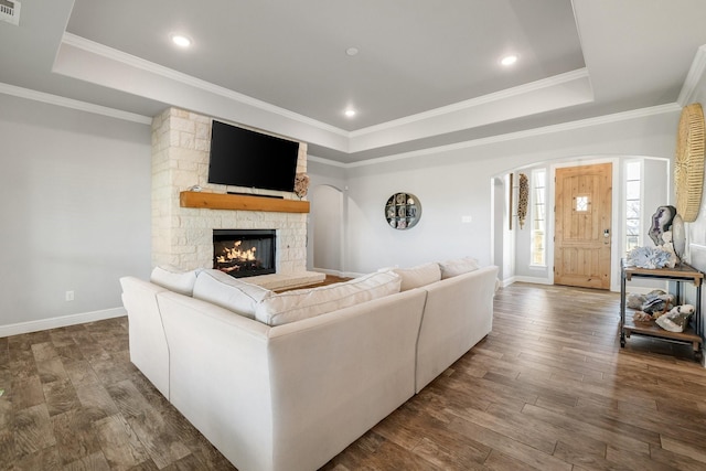 living room featuring a tray ceiling, a fireplace, ornamental molding, and hardwood / wood-style flooring