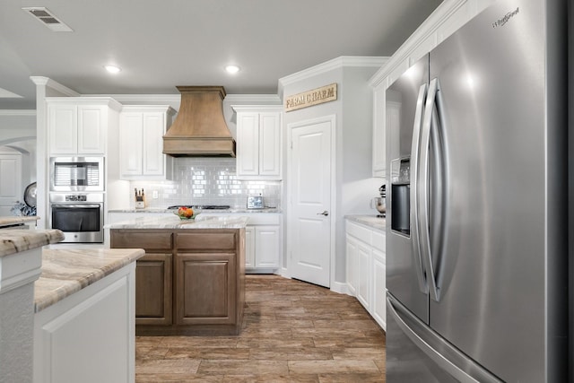 kitchen with custom exhaust hood, appliances with stainless steel finishes, a kitchen island, white cabinetry, and tasteful backsplash