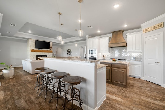 kitchen featuring a large island, a tray ceiling, white cabinetry, and premium range hood