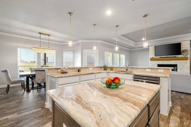 kitchen featuring decorative light fixtures, a kitchen island, a tray ceiling, white cabinetry, and a stone fireplace