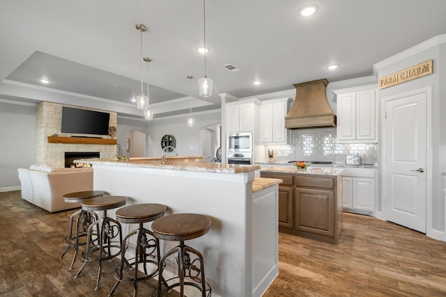 kitchen featuring custom range hood, white cabinetry, a raised ceiling, and a spacious island