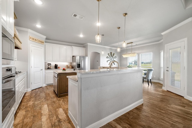 kitchen featuring appliances with stainless steel finishes, decorative light fixtures, white cabinets, dark wood-type flooring, and a center island with sink